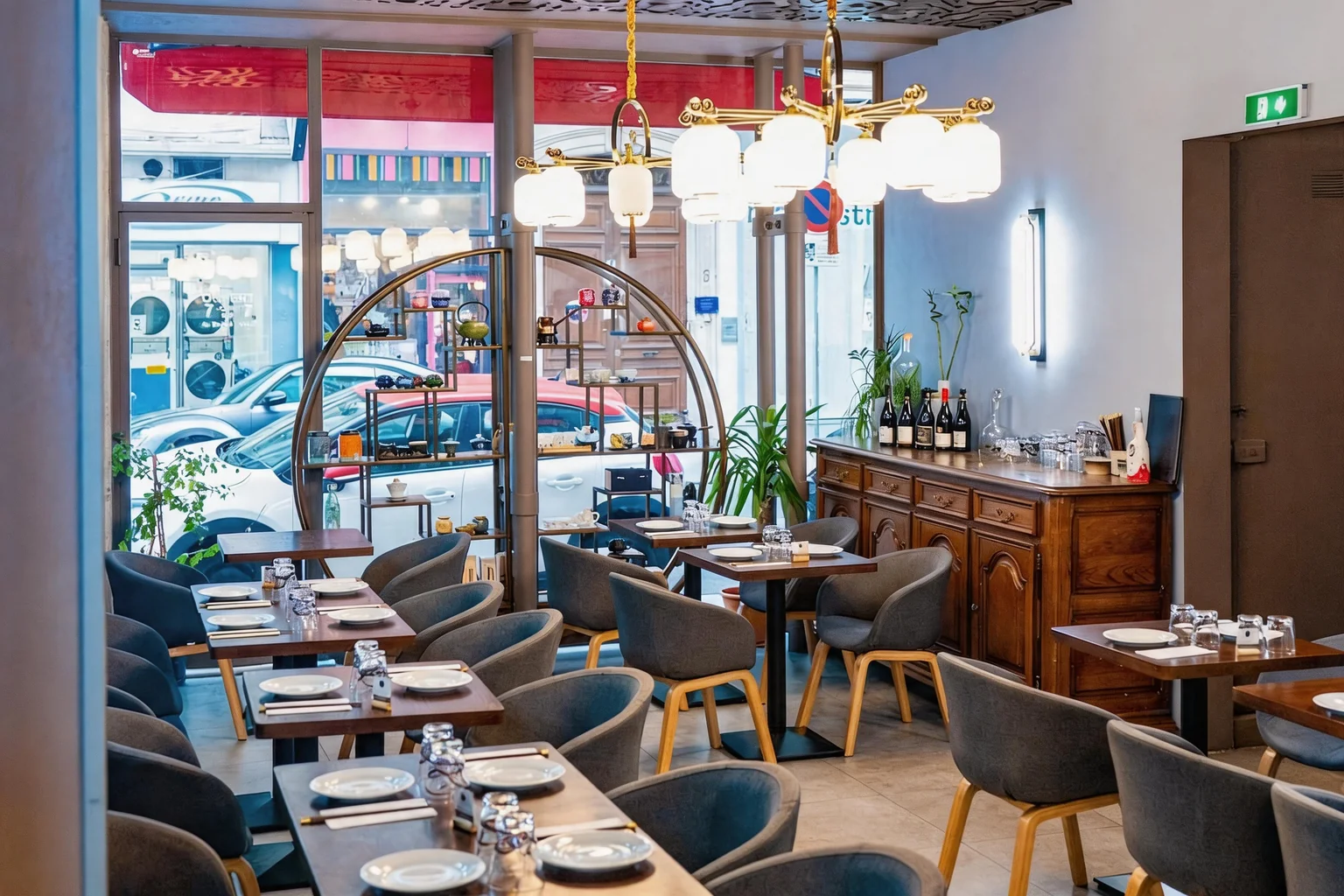 La salle : tables dressées, lustre et étagère ronde devant la vitrine